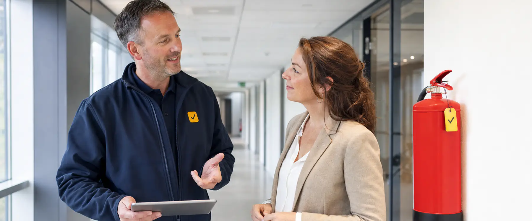 Inspecteur bespreekt de keuring met een facilitair manager in de gang van een kantoorpand
