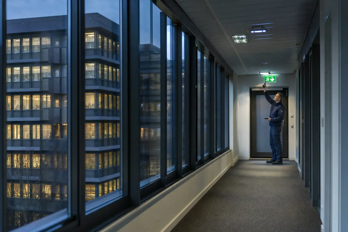 Inspecteur test de noodverlichting in een gang met een groene vluchtwegaanduiding